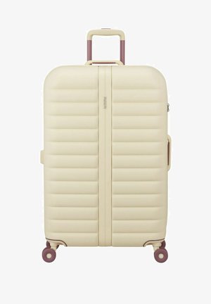 Valise rigide crème avec des nervures horizontales, poignée extensible, poignée latérale et quatre roues pivotantes violettes.