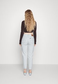Jeans azzurri chiari con vestibilità dritta e cuciture visibili, abbinati a un top nero cropped, visti da dietro. Etichetta del marchio Lee sulla cintura.