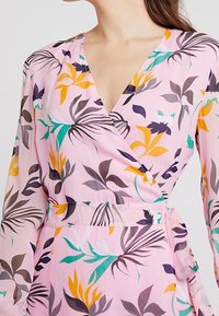 Abito avvolgente rosa con maniche lunghe, caratterizzato da un motivo floreale a foglie nei colori giallo, verde, viola e grigio scuro. Tessuto leggero e fluido.