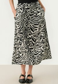 Jupe longue à motif zèbre noir et blanc avec une texture lisse, des poches latérales et une silhouette évasée. Associée à des chaussures noires.