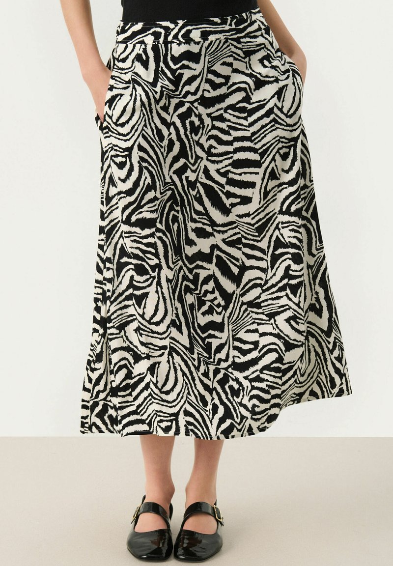 Jupe longue à motif zèbre noir et blanc avec une texture lisse, des poches latérales et une silhouette évasée. Associée à des chaussures noires.