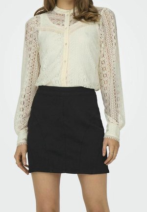 Woman wearing a sheer long-sleeve cream lace blouse with buttons and a high-waist black mini skirt, shown from neck to mid-thigh.