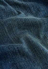 Nahaufnahme von dunkelblauem Denimstoff, der die Struktur und ein diagonales Webmuster mit feinen Falten und Knicken zeigt.
