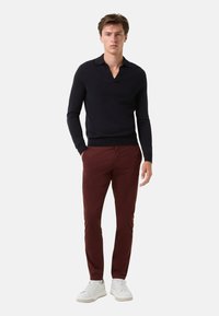 Marineblaues Langarm-Polohemd mit flachem Kragen, kombiniert mit burgunderfarbenen Slim-Fit-Hosen und weißen Sneakers, was einen modernen, lässigen Look kreiert.