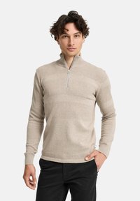 Beige Zip-Up-Pullover mit strukturierten und glatten horizontalen Streifen. Verfügt über lange Ärmel und einen Stehkragen. Getragen mit schwarzen Hosen.