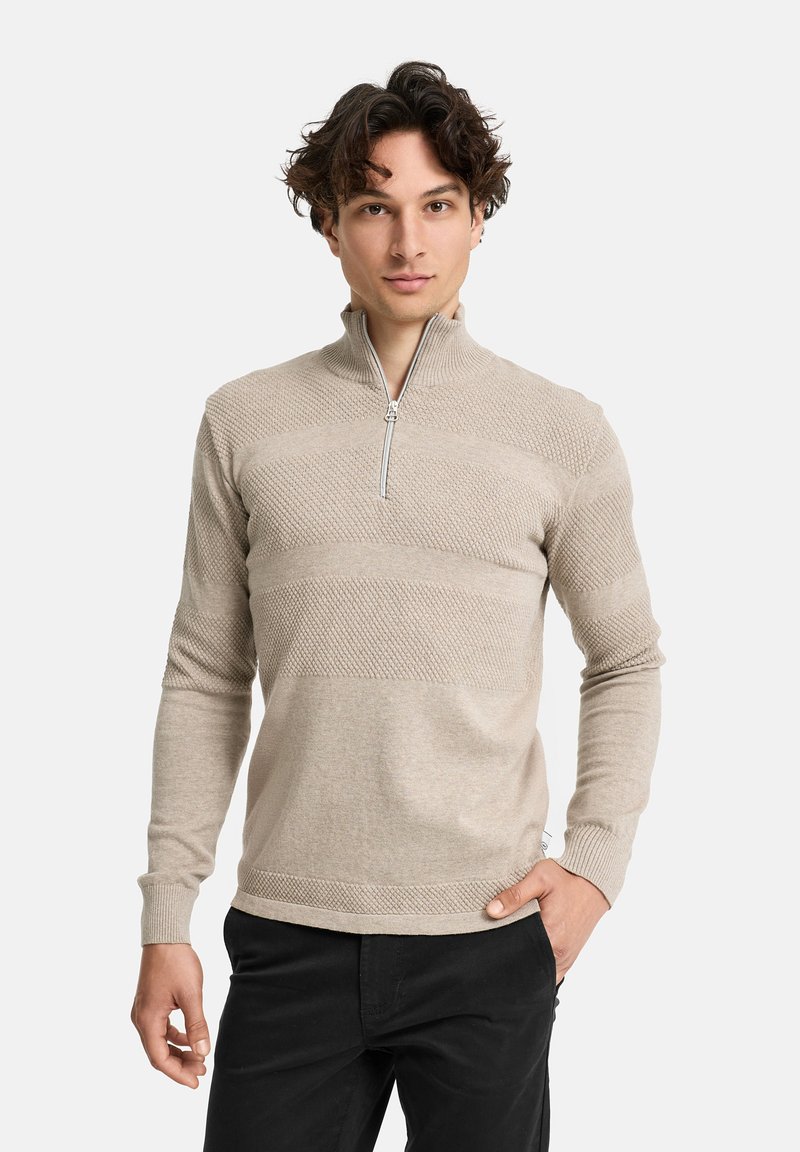 Beige Zip-Up-Pullover mit strukturierten und glatten horizontalen Streifen. Verfügt über lange Ärmel und einen Stehkragen. Getragen mit schwarzen Hosen.