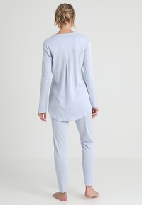 Světle modrý pyžamový set s dlouhým rukávem vyrobený z měkkého materiálu; obsahuje top se zaobleným lemem a úzké kalhoty s manžetami na kotnících.