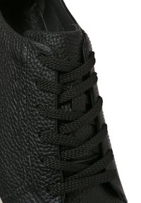 Sneaker nera in pelle, con una superficie testurizzata, lacci neri piatti e un design a profilo basso, dotata di una suola in gomma bianca a contrasto.