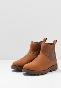 Botas de tobillo de cuero marrón con paneles laterales elásticos, suela de goma texturizada y tira en la parte posterior. Acabado liso con punta redondeada.