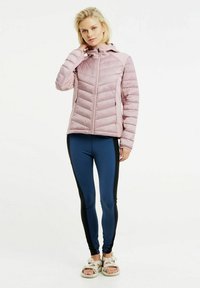 Lichtroze pufferjack met een doorgestikt patroon, vooraan met rits en capuchon. Gecombineerd met marineblauwe leggings met zwarte zijkanten en sandalen.