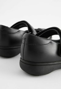 Des chaussures noires en cuir présentent une texture lisse, une forme arrondie et des semelles rembourrées avec des sangles en Velcro pour un maintien sécurisé.