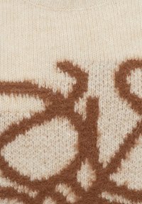 Close-up van beige gebreide stof met fuzzy bruine abstracte vormen die in de textuur zijn geweven.