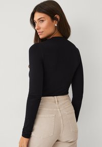 Schwarzes Langarmoberteil mit körperbetonter Passform, kombiniert mit hellbeigen, hoch taillierten Jeans mit Gesäßtaschen und glatter Textur.