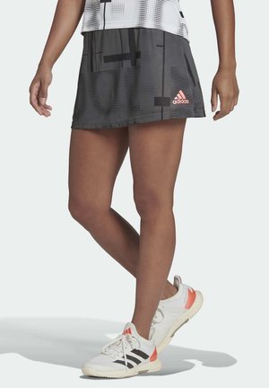 Zwarte sportrok met geometrische patronen; heeft een roze Adidas-logo. Draagt met witte schoenen, wat een comfortabele ontwerpe en pasvorm laat zien.