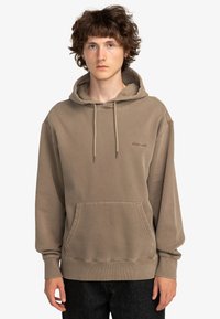 Beige sweatshirt med huva i mjukt tyg. Har en framficka, dragsko i huvan och en diskret logotyp i matchande färg på bröstet.