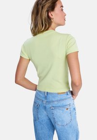 Jasnozielona, krótka koszulka wykonana z miękkiej bawełny. Posiada krótkie rękawy i okrągły dekolt. Połączona z jasnoniebieskimi dżinsami z wysokim stanem.