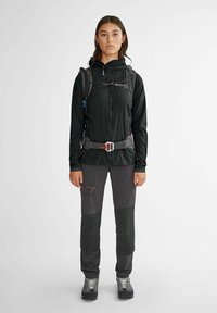 Veste zippée noire et pantalon de randonnée gris foncé avec des renforts aux genoux. La veste présente une coupe ajustée et un sac à dos avec accès à l'hydratation.