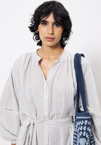 Gestreiftes Button-Down-Kleid mit gerafftem Halsausschnitt und Puffärmeln, mit einem Knoten in der Taille. Accessoires sind eine blaue gehäkelte Handtasche.