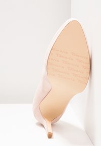 Chaussure à talon haut en daim rose avec bout pointu et talon fin. La semelle présente un motif discret du nom de la marque embossé.