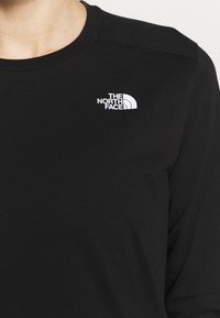 Schwarzes Langarmshirt mit Rundhalsausschnitt und Flachnaht, ausgestattet mit einem kleinen weißen Logo auf der linken Brust. Glatte Stofftextur.