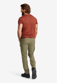 Rostfärgad t-shirt med kort ärm i kombination med olivgrön cargobyxa; funktionella fickor, justerbara ärmslut och robusta svarta skor.