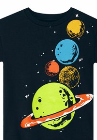 Camiseta negra con gráficos de planetas coloridos: planeta verde con anillos, planetas azul, naranja, amarillo y texturizados sobre un fondo estrellado.