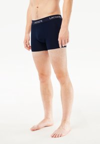 Boxer briefs azul marinho feitos de um tecido suave com um ajuste justo, apresentando uma cintura com o logótipo Lacoste e pernas curtas. Sem padrões adicionais.