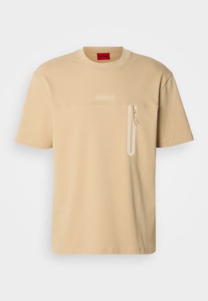 T-shirt beige con scollo rotondo, maniche corte e tasca con zip sul petto. Logo testuale di colore chiaro sopra la tasca.