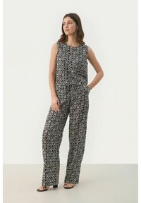 Tuta stampata in bianco e nero con un design senza maniche, vestibilità ampia, gambe larghe e vita con cordino, caratterizzata da un motivo a spirale.