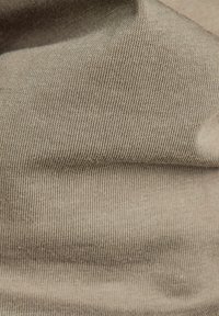 Zbliżenie beżowej dzianiny z widocznymi drobnymi ściegami i miękkimi fałdami.