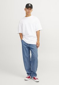 Camiseta blanca de gran tamaño, vaqueros azules holgados, zapatillas rojas y blancas. Gorro negro con gráfico del sol. Conjunto sencillo y casual con patrones mínimos.