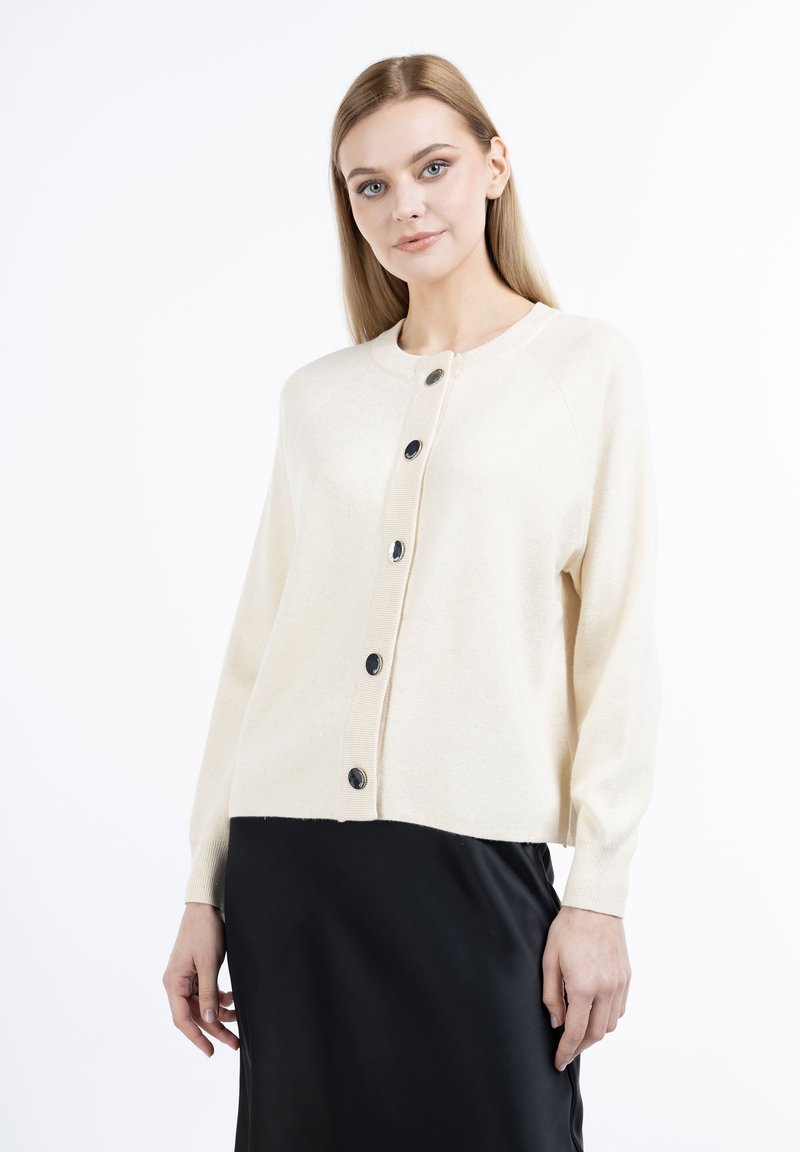 Cardigan crema realizzato in materiale morbido e leggero. Presenta polsini a coste, colletto rotondo e sei bottoni neri lucidi sul davanti.