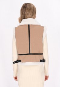 Bruine vest met een faux schapenvacht kraag en achterkant, voorzien van zwarte banden, een gladde textuur en een getailleerd ontwerp.