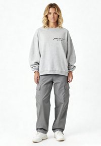 Sweat-shirt gris avec "suis ton cœur" brodé en noir, accompagné d'un pantalon cargo gris ample avec poches, et de baskets blanches.