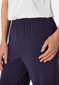 Hosen mit elastischem Bund in Marineblau aus glattem Stoff. Nahaufnahme, die eine Hand auf dem Oberschenkel zeigt und den Komfort sowie die Passform betont.