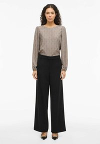 Šviesiai ruda raštuota palaidinė su ilgomis rankovėmis, derinama prie aukšto liemens juodų plačių kelnių ir juodų smailių batelių su aukso detalėmis.