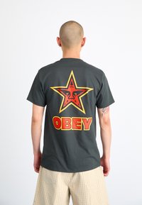 Gray cotton t-shirt with a large red and yellow star graphic and "OBEY" text on the back. Short sleeves and a standard fit.