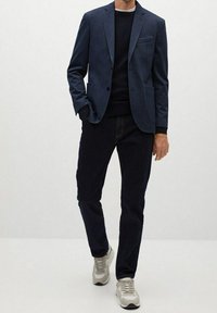 Marynarka w morskim kolorze z subtelną fakturą, nałożona na ciemny sweter. Połączona z ciemnymi dżinsami i jasnoszarymi sneakersami. Prosty, nowoczesny design.