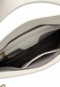 Interno di una borsa a mano in pelle bianca con una singola tasca con zip, fodera morbida e due tasche a scomparsa per l'organizzazione. Materiale testurizzato.