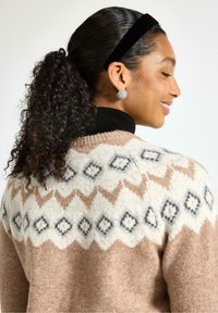 Strikket sweater i beige med et tekstureret design, der har diamant- og zigzag-mønstre i lys brun og grå. Sort krave detaljer synlig.