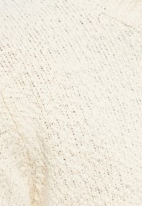 Primeiro plano de um tecido de malha off-white com um padrão texturizado de cabos e pequenos buracos dispostos em linhas diagonais e verticais.