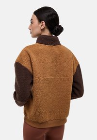 Veste en polaire marron et beige avec un col haut, tissu texturé et manches contrastées ; ourlet côtelé ; coupe décontractée, portée de dos.