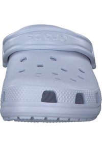 Zueco de plástico blanco con agujeros de ventilación, correa en el tobillo y suela texturizada. Superficie lisa con bordes redondeados. Diseño ligero y duradero.
