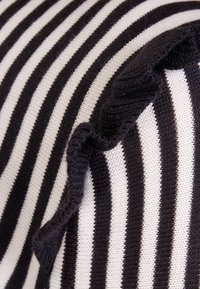 Tessuto a righe bianche e nere con dettaglio di bordo arricciato. La texture appare morbida e lavorata a maglia, con strisce alternate larghe e strette.