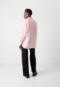 Rosa bomullsskjorta med avslappnad passform, långa ärmar och rundad nederkant, perfekt i kombination med svarta byxor med vida ben som har subtila glittrande detaljer.