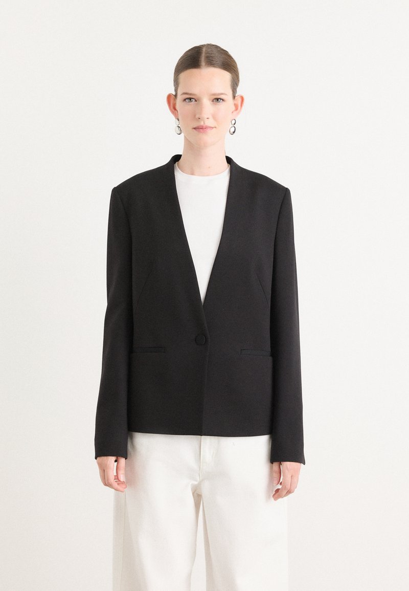 Blazer nero con design a V, maniche lunghe e chiusura a un bottone. Presenta due tasche frontali e una texture di tessuto liscia.