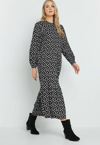 Vestido negro con lunares, mangas globo largas, escote redondo y dobladillo acampanado. Combinado con botas negras hasta el tobillo.