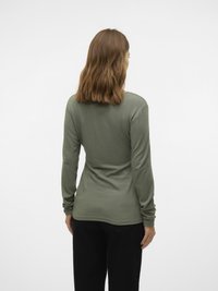 Majica z dolgimi rokavi v olivno zeleni barvi, narejena iz teksturirane tkanine. Ima oprijeto obliko s rahlo ukrivljenim robom in ozkimi rokavi.