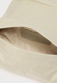 Μπεζ δερμάτινη τσάντα ανοιχτή που δείχνει το απαλό ύφασμα επένδυσης και την ραμμένη ετικέτα της μάρκας Diesel στο εσωτερικό.