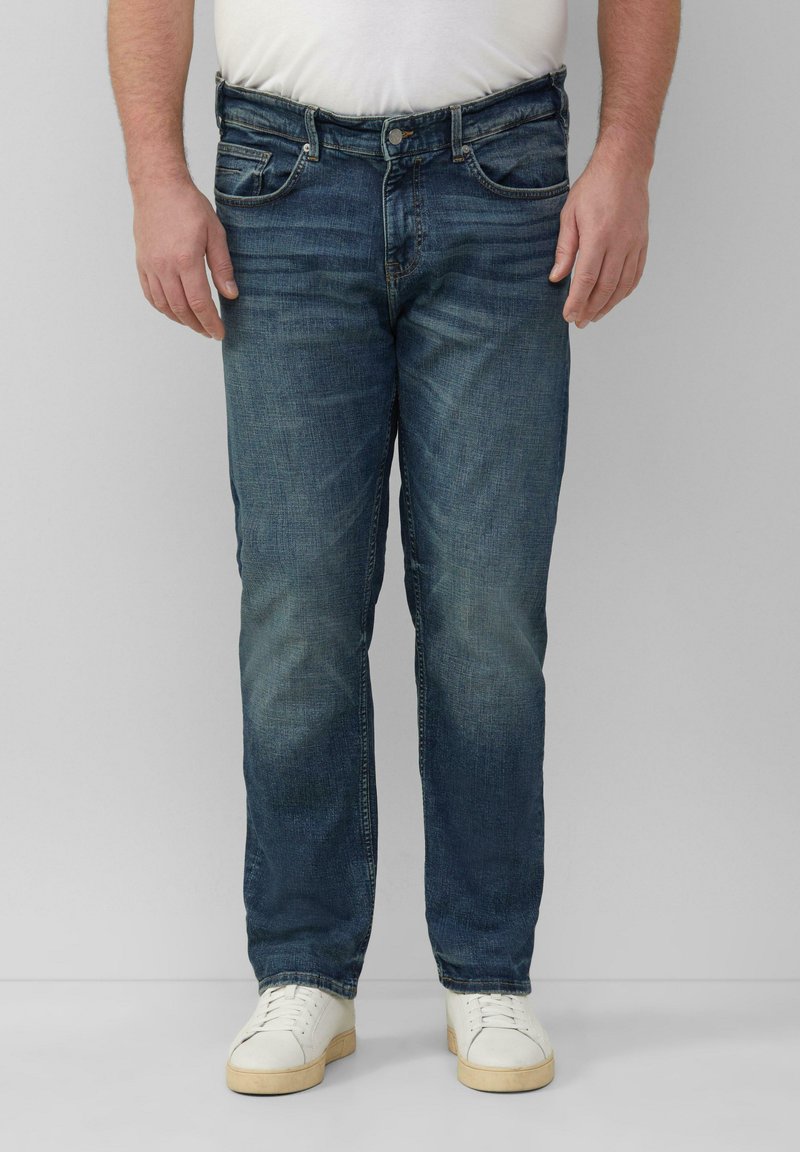 Blaue Jeans aus Denim mit geradem Schnitt, fünf Taschen und subtiler Ausbleichung an den Oberschenkeln, kombiniert mit weißen Sneakers.